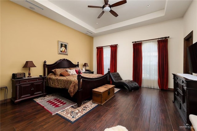 bedroom with ceiling fan, dark wood-type flooring, and a tray ceiling