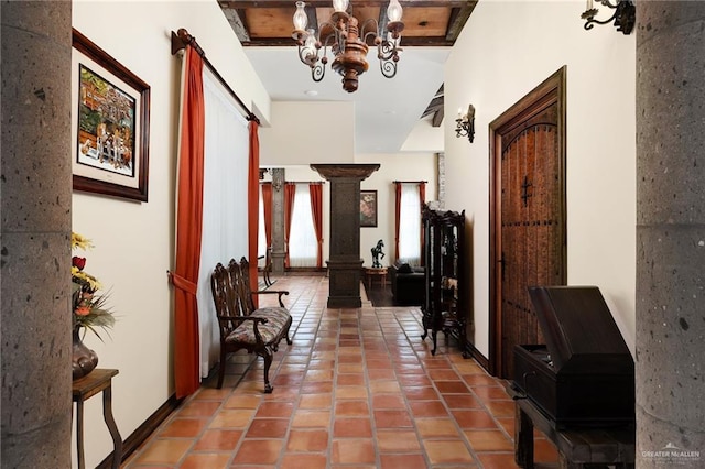 hallway featuring tile patterned flooring, an inviting chandelier, ornate columns, and beamed ceiling