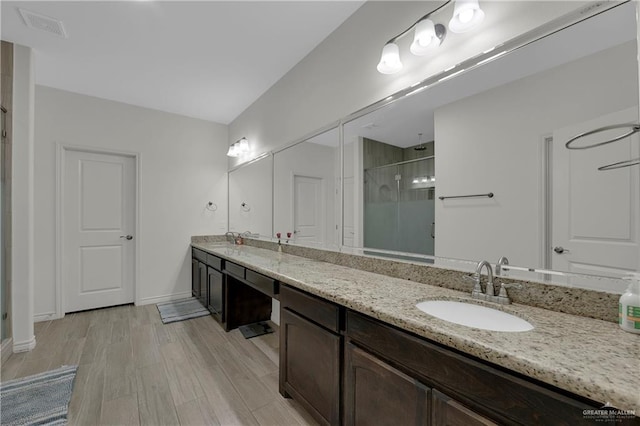 full bathroom featuring double vanity, a shower stall, a sink, and wood finished floors