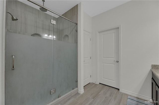 full bathroom with a stall shower, vanity, baseboards, and wood finished floors