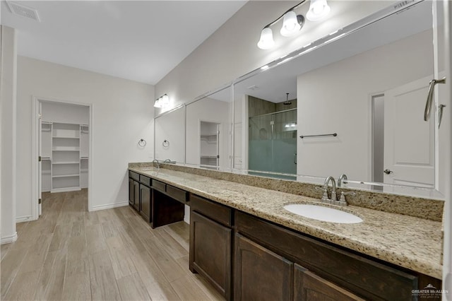 full bathroom featuring a walk in closet, double vanity, a stall shower, a sink, and wood finished floors