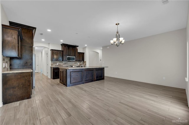 kitchen with arched walkways, dark brown cabinetry, light countertops, hanging light fixtures, and stainless steel microwave