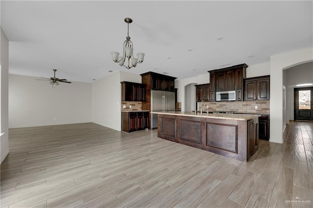 kitchen featuring dark brown cabinetry, appliances with stainless steel finishes, a kitchen island with sink, pendant lighting, and a sink