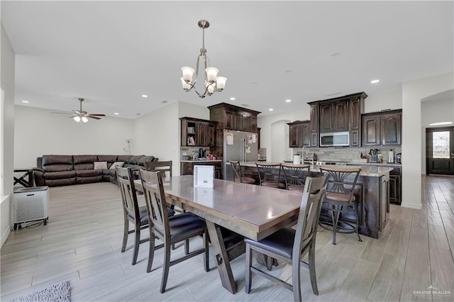 dining space with ceiling fan with notable chandelier, recessed lighting, arched walkways, and light wood-style floors