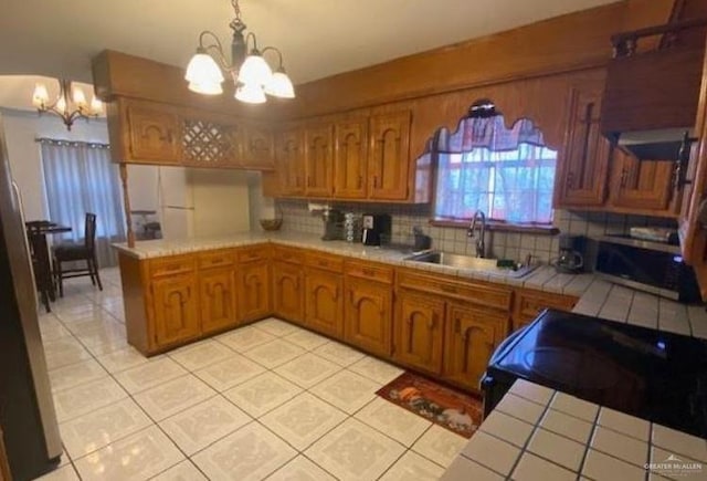 kitchen featuring kitchen peninsula, backsplash, sink, tile countertops, and an inviting chandelier