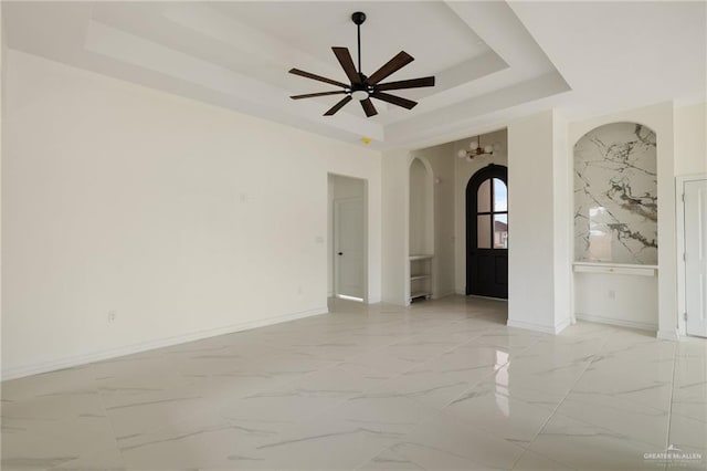 spare room with arched walkways, a raised ceiling, marble finish floor, and baseboards