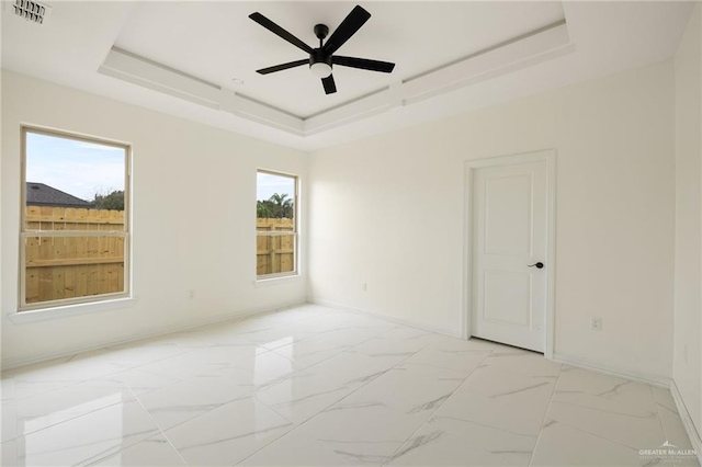 unfurnished room with a wealth of natural light, marble finish floor, a tray ceiling, and visible vents