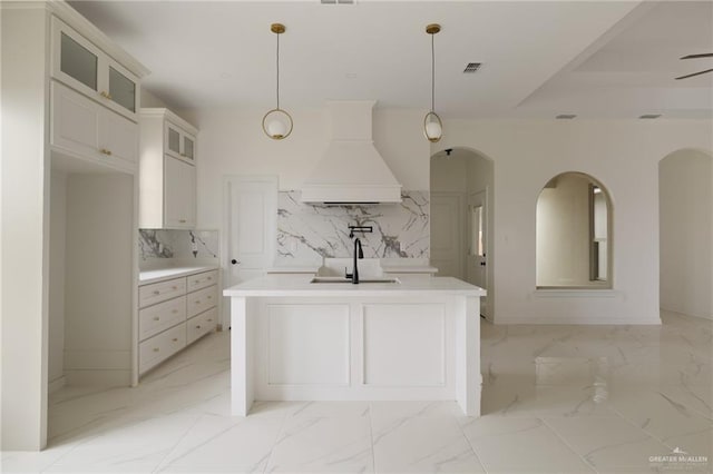 kitchen with marble finish floor, light countertops, custom range hood, glass insert cabinets, and a sink