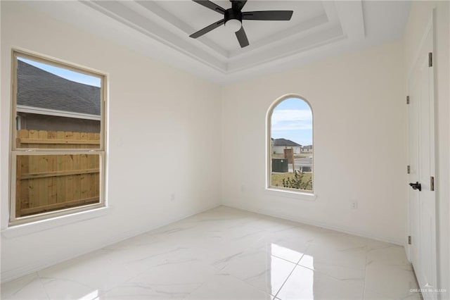 unfurnished room featuring ceiling fan, marble finish floor, a raised ceiling, and baseboards