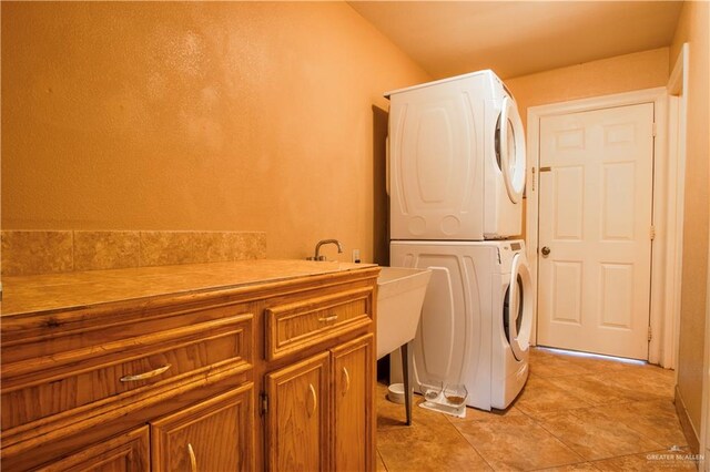 laundry room featuring cabinets, light tile patterned floors, and stacked washing maching and dryer