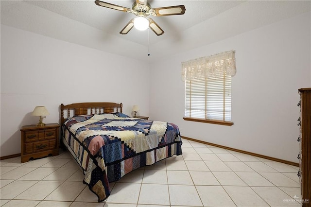 bedroom featuring a raised ceiling, light tile patterned flooring, baseboards, and ceiling fan