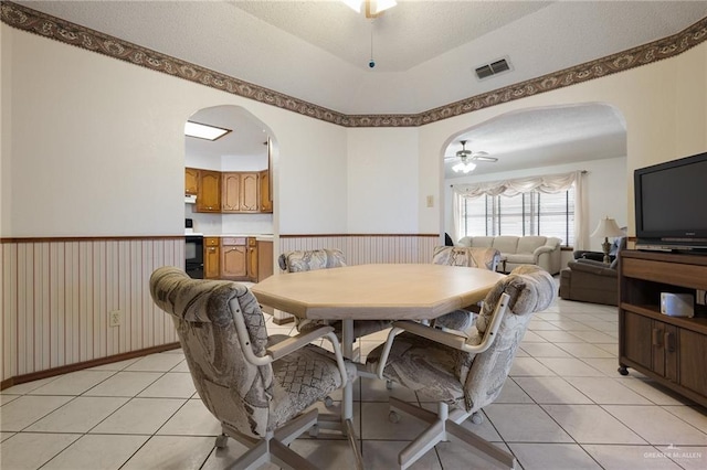 dining space with visible vents, arched walkways, a ceiling fan, and wainscoting