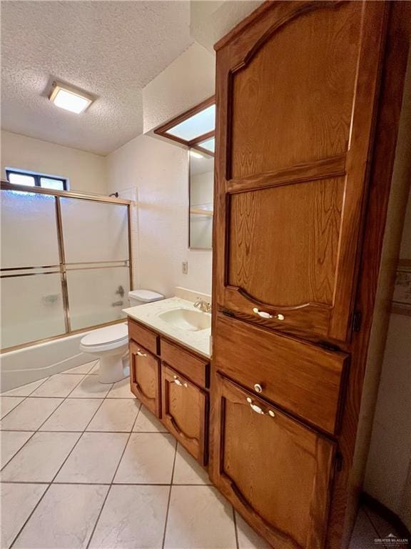 full bath with bath / shower combo with glass door, toilet, vanity, tile patterned floors, and a textured ceiling