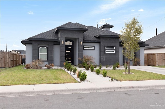 prairie-style house with a front lawn, fence, roof with shingles, and stucco siding