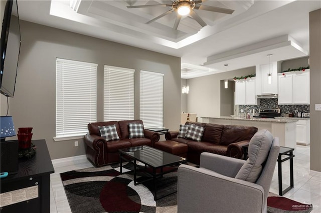 living room with baseboards, light tile patterned floors, a ceiling fan, and a tray ceiling