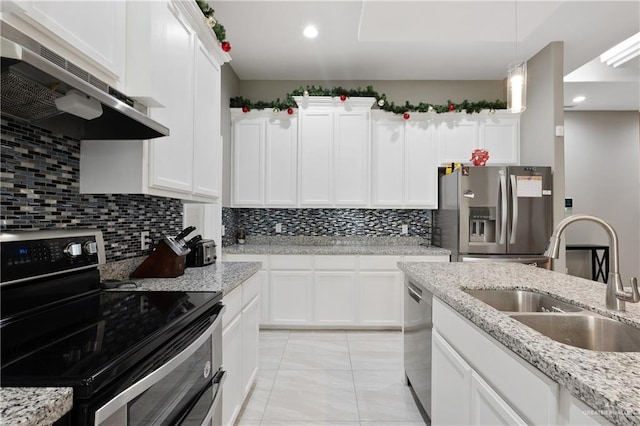 kitchen with under cabinet range hood, decorative backsplash, appliances with stainless steel finishes, white cabinetry, and a sink