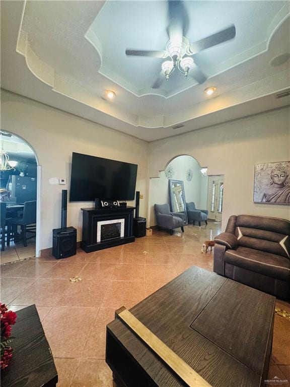 tiled living room featuring arched walkways, a raised ceiling, visible vents, ceiling fan, and baseboards