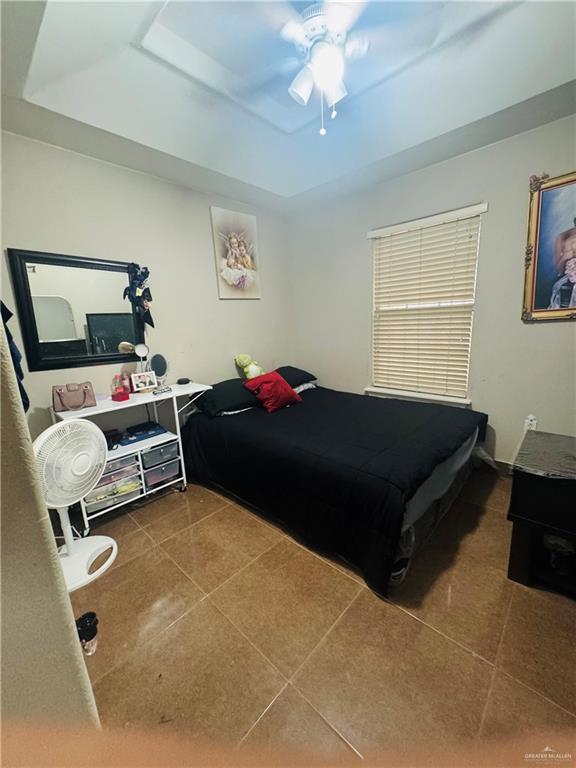 tiled bedroom with ceiling fan and a raised ceiling