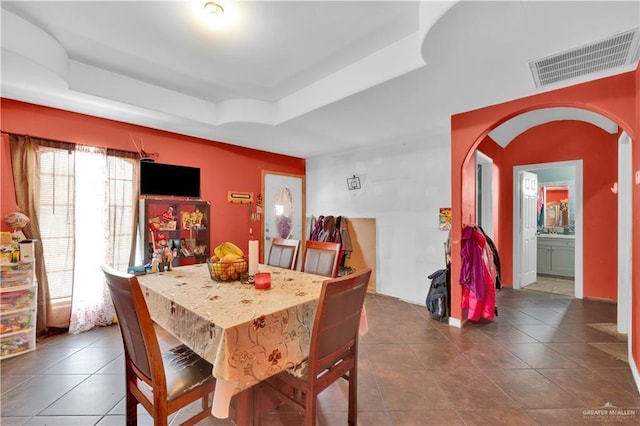 dining area with arched walkways, dark tile patterned flooring, a raised ceiling, and visible vents