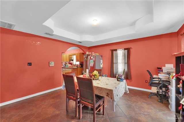 dining space with arched walkways, a raised ceiling, visible vents, and baseboards