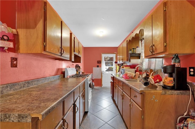 kitchen featuring light tile patterned floors, a sink, brown cabinets, and white range with gas cooktop