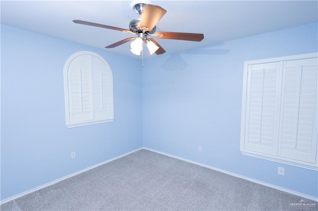 carpeted spare room featuring baseboards and a ceiling fan