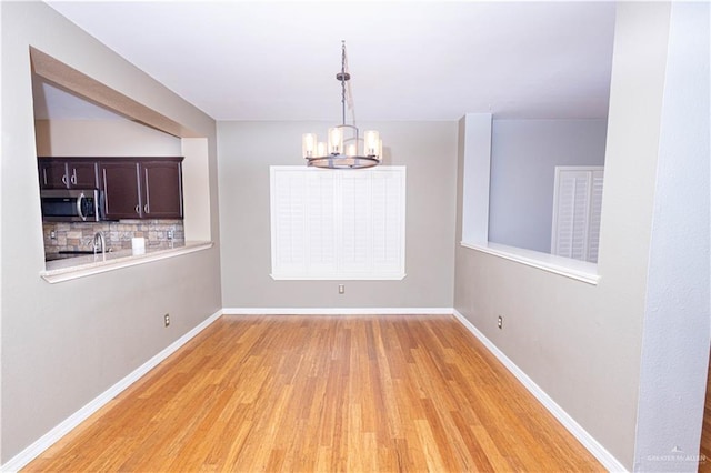 unfurnished dining area featuring baseboards, light wood-style floors, and a notable chandelier