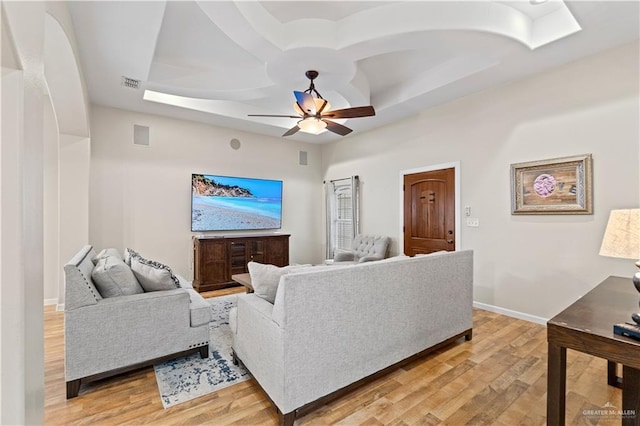 living room featuring light hardwood / wood-style floors, a raised ceiling, and ceiling fan