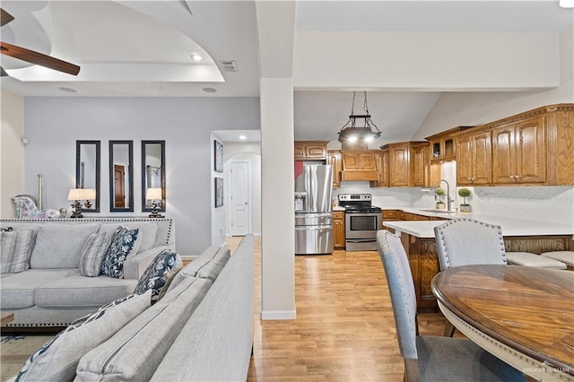 kitchen with appliances with stainless steel finishes, hanging light fixtures, a kitchen breakfast bar, sink, and light wood-type flooring