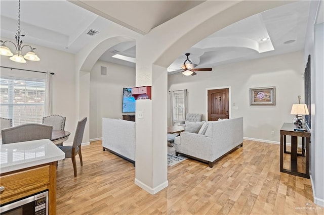 living room with light hardwood / wood-style floors, a tray ceiling, and ceiling fan with notable chandelier