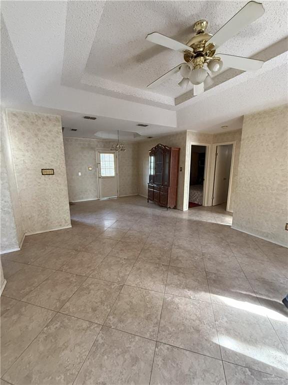 tiled empty room with ceiling fan with notable chandelier, a tray ceiling, and a textured ceiling