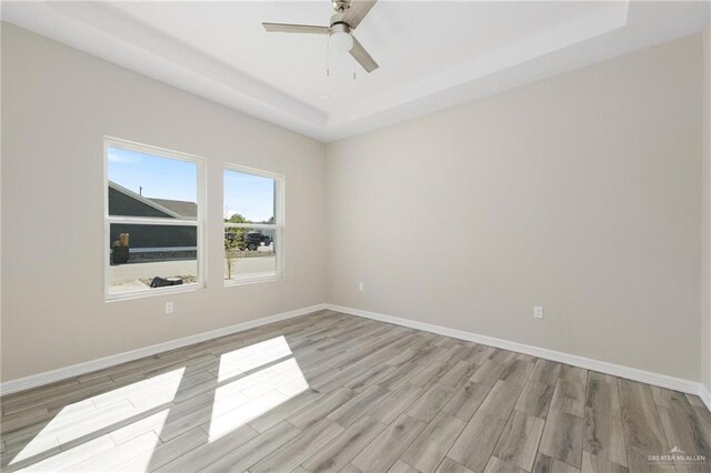 empty room with light wood-style floors, a raised ceiling, and baseboards