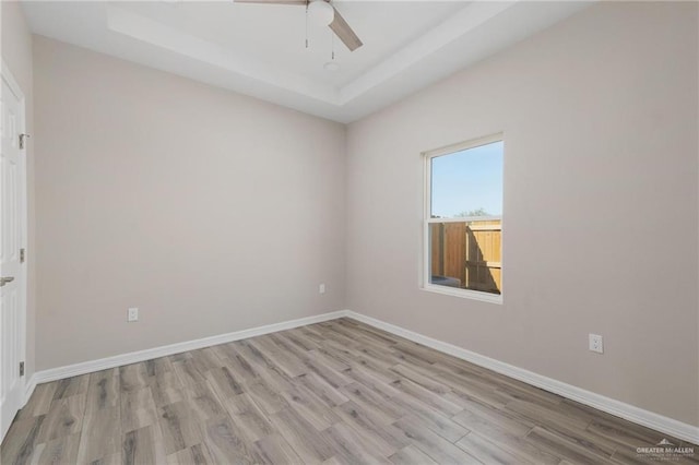 empty room with a raised ceiling, ceiling fan, light wood finished floors, and baseboards