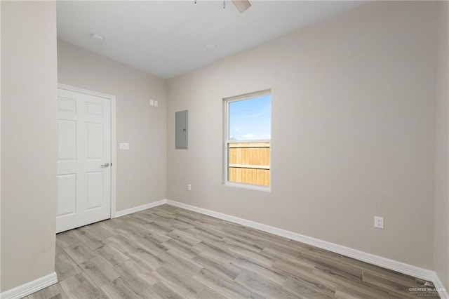 spare room featuring light wood-type flooring, electric panel, baseboards, and a ceiling fan