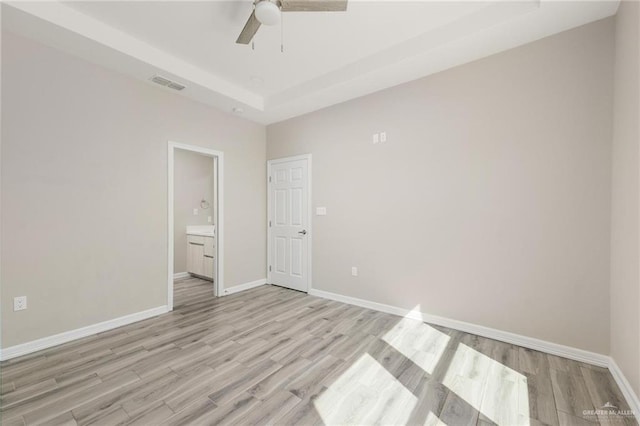 unfurnished bedroom featuring light wood-style floors, a raised ceiling, visible vents, and baseboards