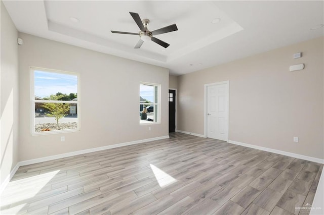 empty room with a raised ceiling, light wood-style flooring, and baseboards