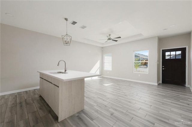 kitchen featuring an island with sink, open floor plan, hanging light fixtures, light countertops, and a sink