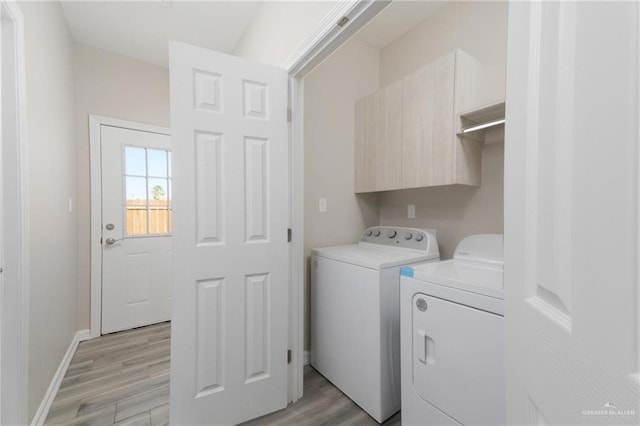 laundry area featuring baseboards, cabinet space, light wood finished floors, and washing machine and clothes dryer