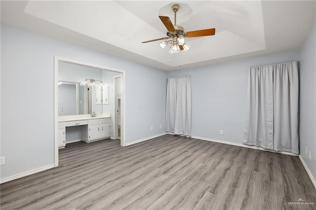 unfurnished bedroom featuring light wood-style floors, a tray ceiling, a sink, and baseboards