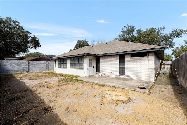 back of property with brick siding, a fenced backyard, a shingled roof, and a patio