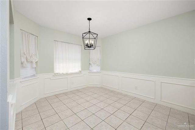 spare room featuring a chandelier, light tile patterned floors, and a wainscoted wall