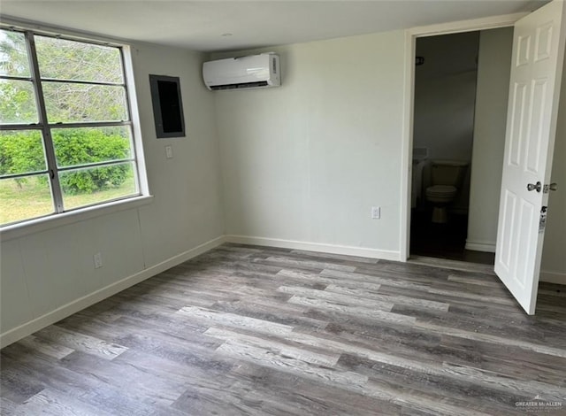 empty room featuring a wall mounted air conditioner, baseboards, and wood finished floors