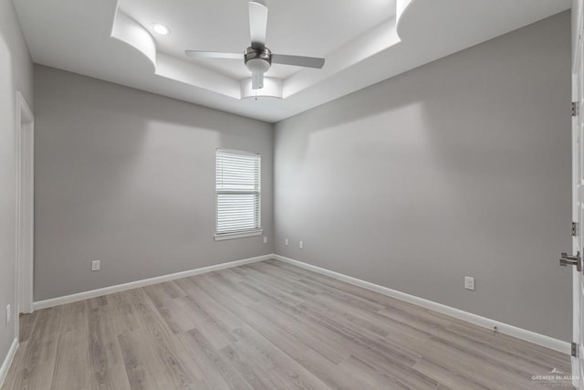 empty room featuring a raised ceiling, light hardwood / wood-style flooring, and ceiling fan