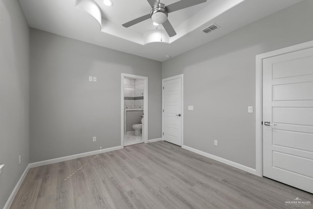 empty room with a tray ceiling, ceiling fan, and light wood-type flooring