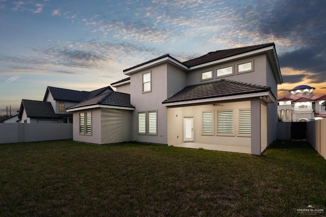 back house at dusk featuring a lawn and ceiling fan