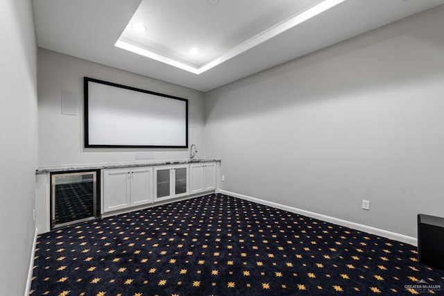 carpeted home theater room with sink, a raised ceiling, and wine cooler