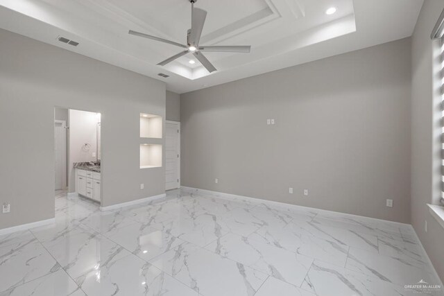 unfurnished bedroom featuring a raised ceiling, ensuite bathroom, and ceiling fan