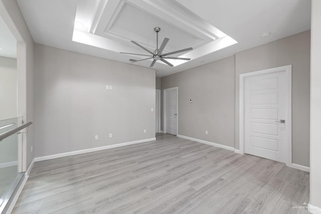 spare room with ceiling fan, light wood-type flooring, and a raised ceiling