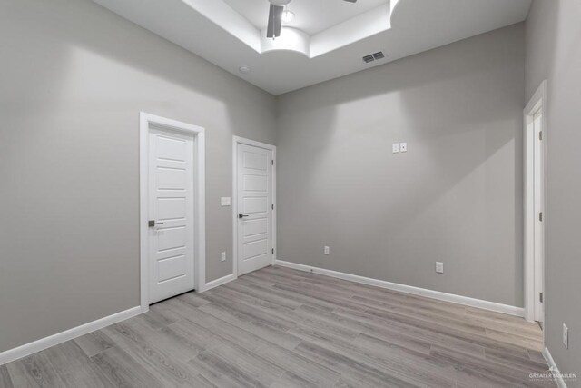 spare room with ceiling fan, light hardwood / wood-style floors, and a raised ceiling