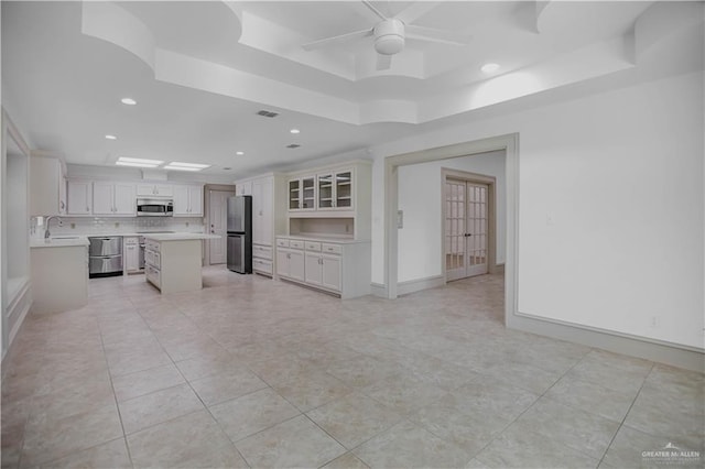 kitchen with appliances with stainless steel finishes, a raised ceiling, a sink, light countertops, and a center island